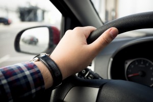 Closeup shot of male hand in watches holding car steering wheel